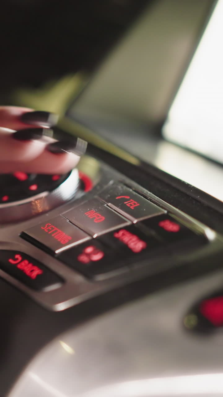 First-person view of a woman's hand pressing the Tel button on a car control panel at night. The dashboard is illuminated with red lights, highlighting the controls. Shot with a handheld camera