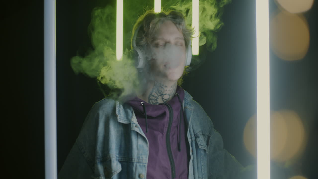 Man with headphones and tattoos, smoking vaporizer in neon lights