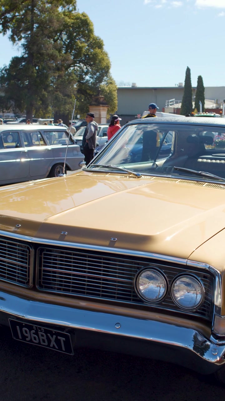 Klassisches goldenes Auto fährt langsam an Menschen und Imbisswagen vorbei auf einem hellen Outdoor-Markt.