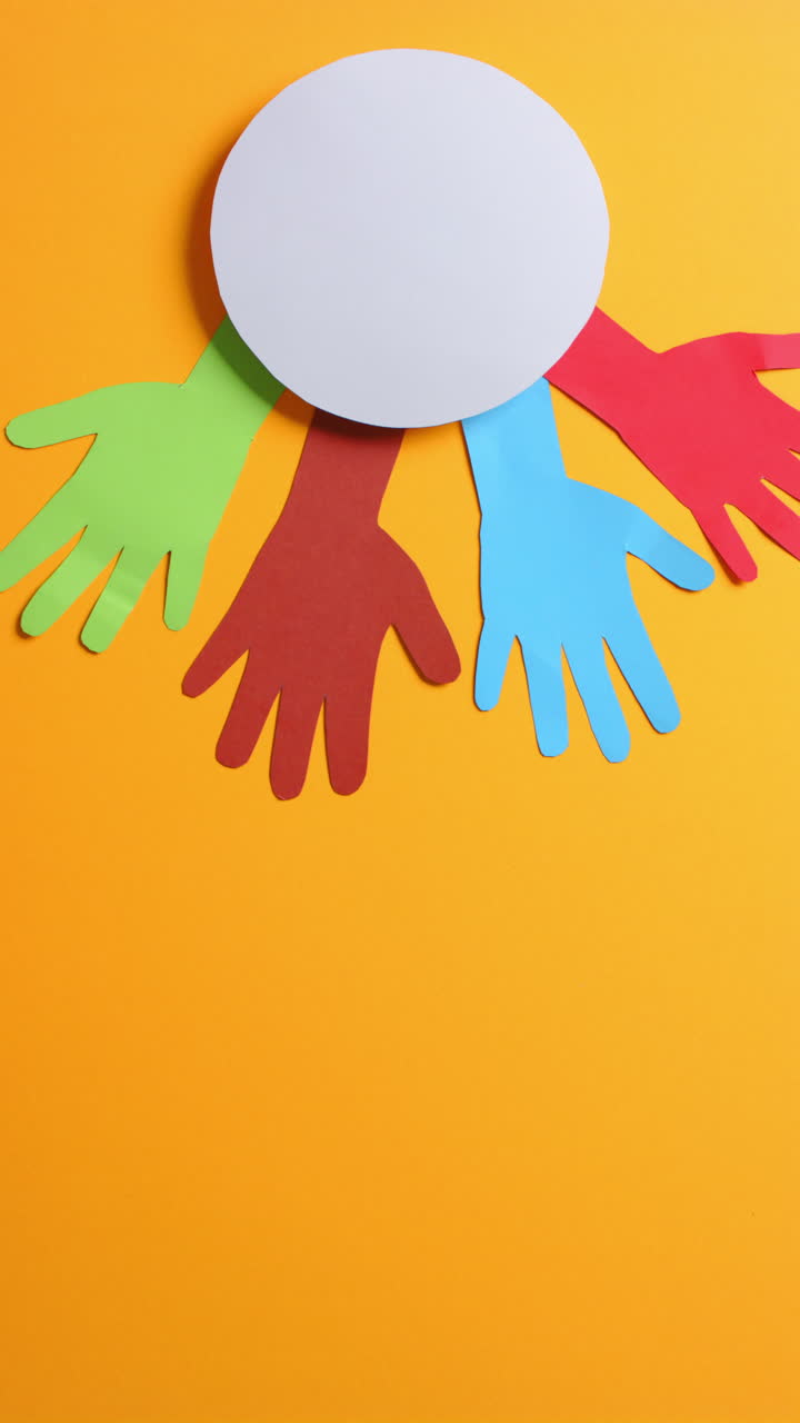 Vertical video of hands around circle made of colourful paper on orange background with copy space