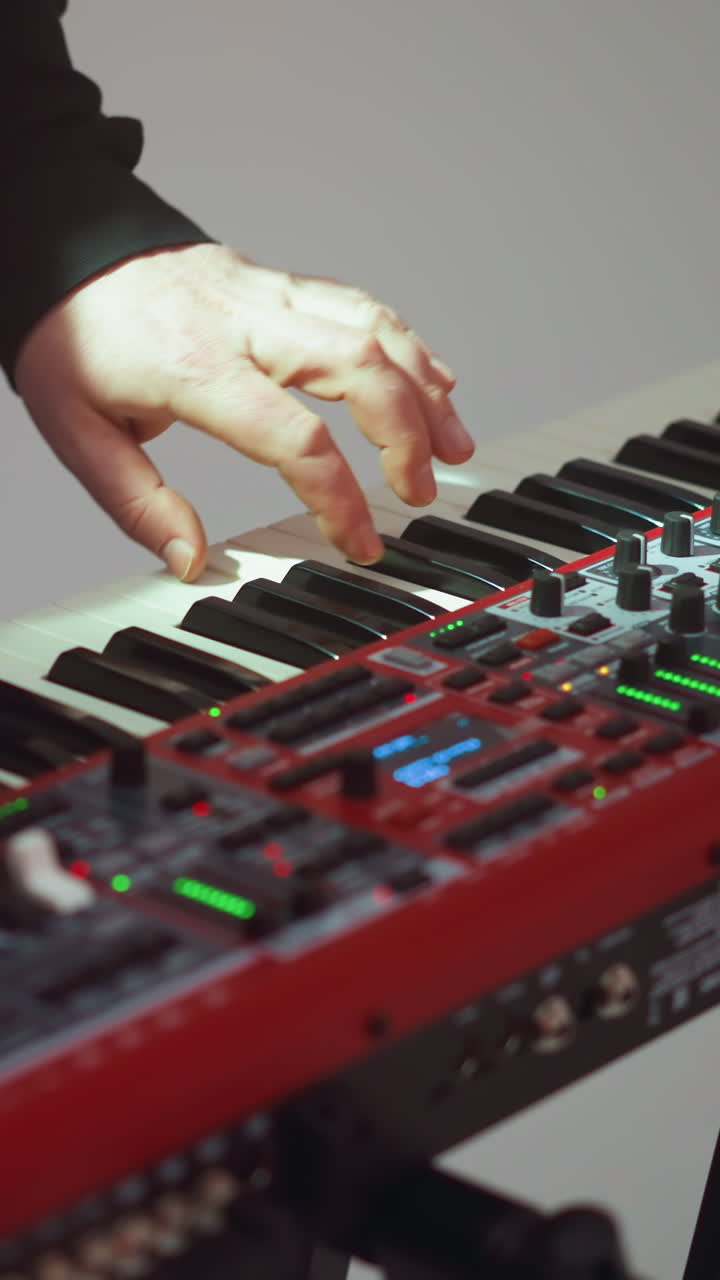 Close view of a hand playing a red sampler piano against a plain white background, highlighting the focus on the instrument and the musicians fingers in motion