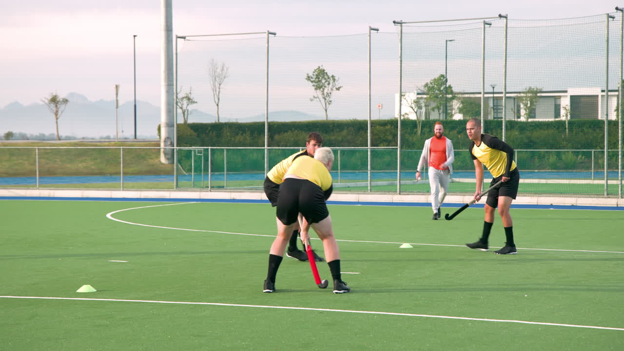 Playing field hockey, male athletes in yellow jerseys practicing on green field