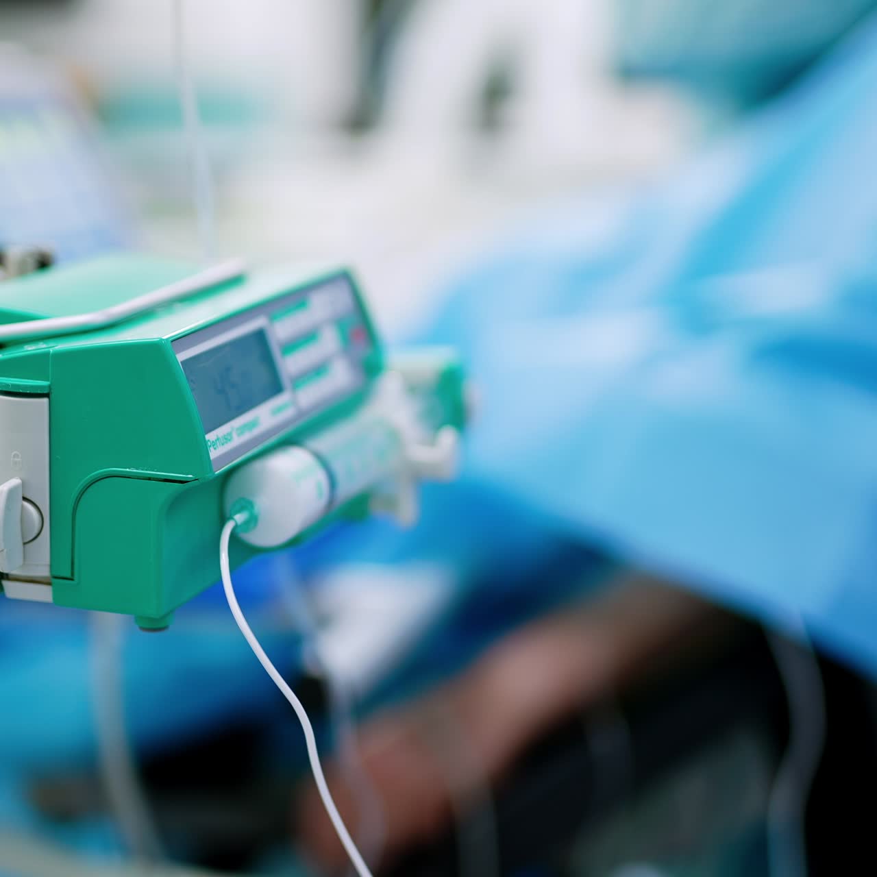 Dispositivo per infusione di farmaci in sala operatoria. Paziente sotto anestesia sullo sfondo, in versione sfocata.