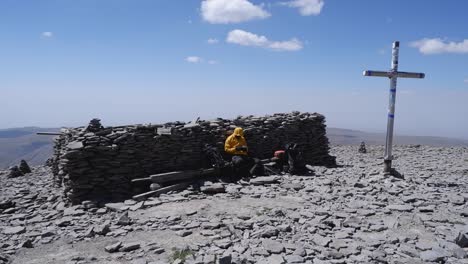 Climber-rests-by-huge-stone-cairn-near-crucifix-on-mountain-summit