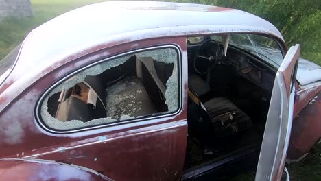 Old-rusty-red-beetle-car-sitting-in-a-grassy-field-on-a-sunny-day-during-the-summer-with-a-blue-sky-and-clouds-overhead