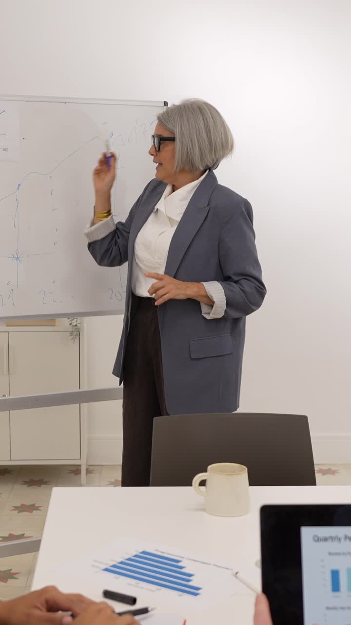 Mature Businesswoman Explaining Graphs on Whiteboard During Office Meeting