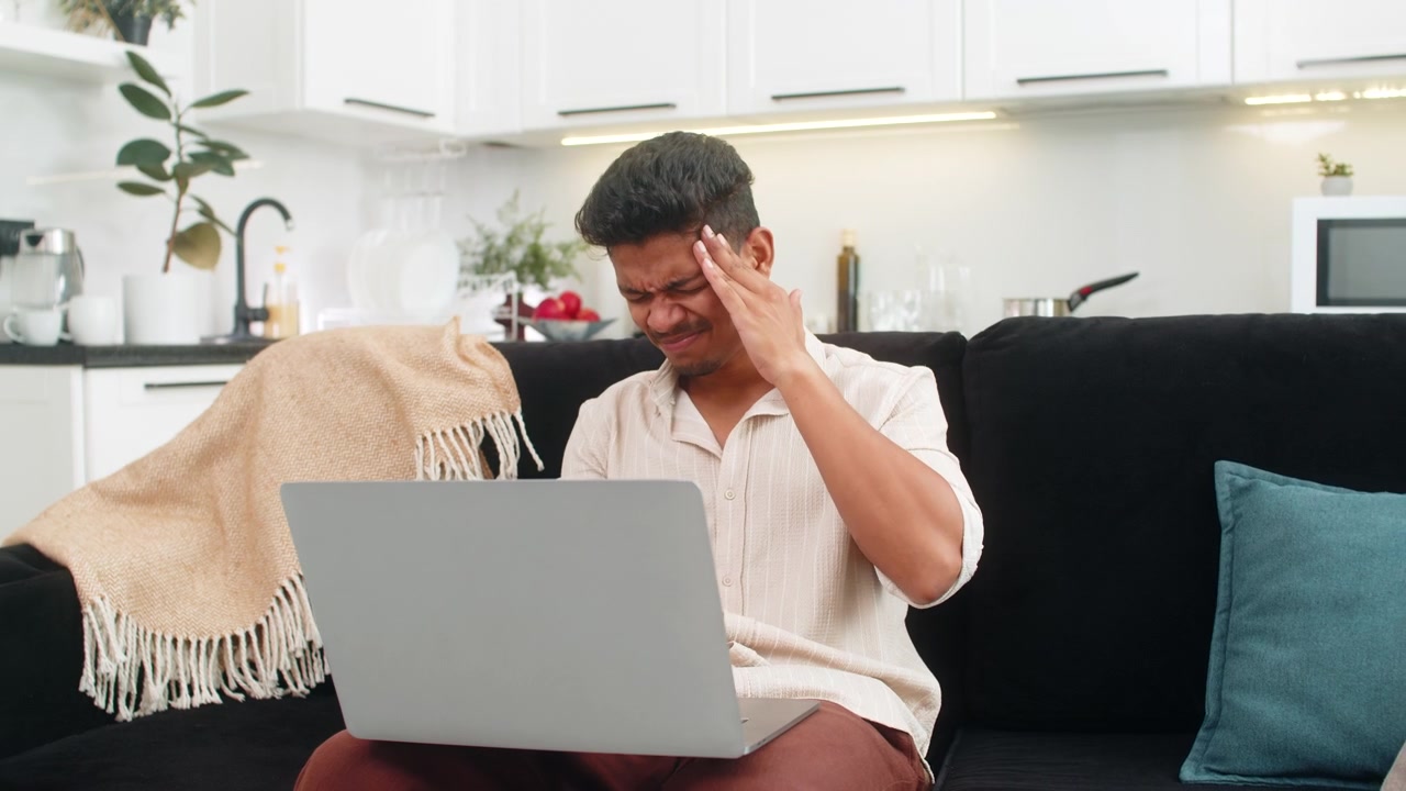 Indian man rubs temples from laptop glare does breath exercise and returns to work with calm focus