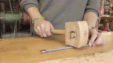 close up of a male working on jewelry with a large wooden hammer