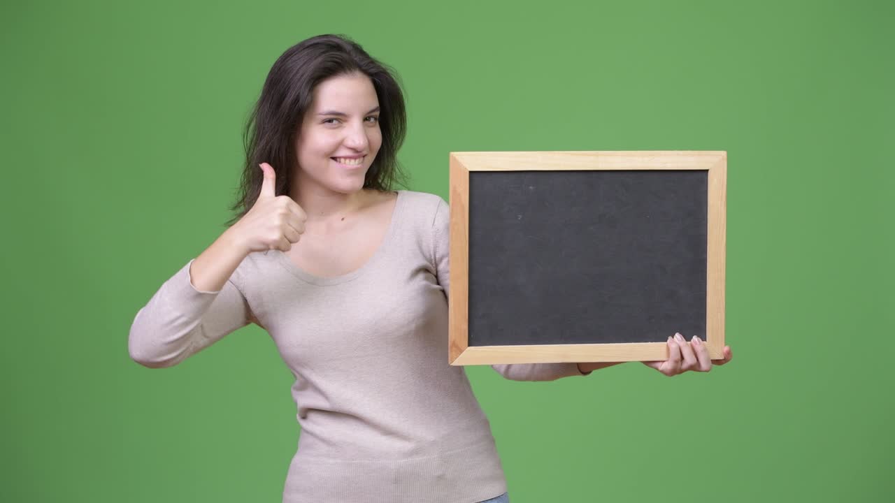 Young happy beautiful woman giving thumbs up while holding blackboard