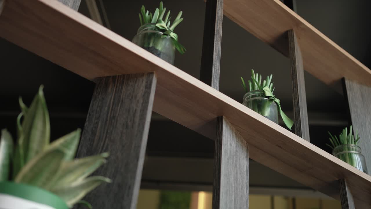 small green plants in glass jars displayed on a diagonal wooden shelf in indoor modern space