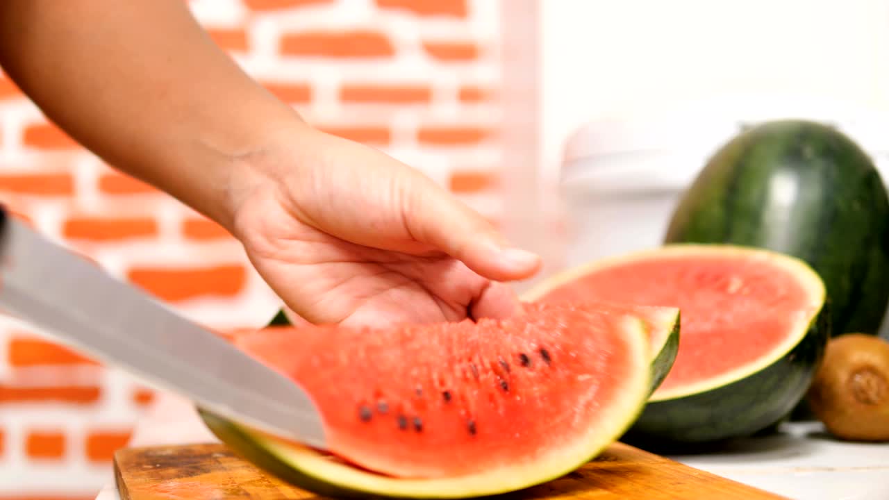 manos de mujeres usando un cuchillo cortan la sandía en pedazos en una tabla de madera en una cocina