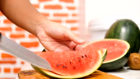 hands of women using a knife slice the water melon into pieces on wooden board in a kitchen