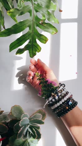 mano con pulseras y flores entre las plantas