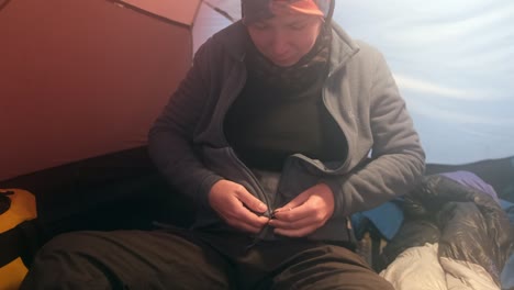 a girl in a tent sits and puts on a warm fleece jacket before climbing
