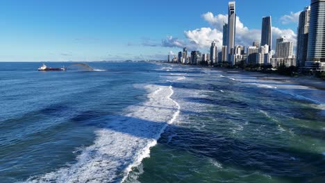 Drone captures sand dredging along Gold Coast beach with city skyline, blue ocean, and clear skies