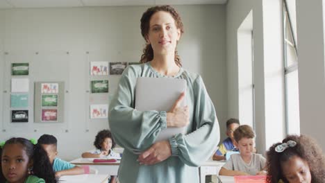 Vídeo-De-Una-Feliz-Profesora-Caucásica-Sosteniendo-Una-Computadora-Portátil-En-Una-Clase-De-Alumnos-Diversos