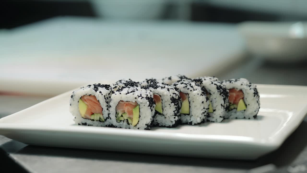 Sushikokki käsineet kädessä asettaa rullat koristellulle lautaselle sushibaarissa. Ammattikokki valmistaa rullia asiakkaalle ammattikeittiössä.