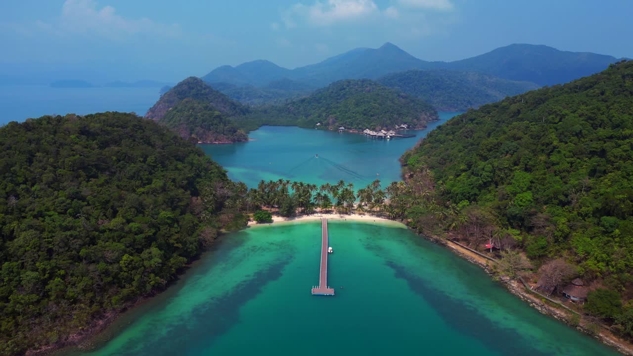 Koh Chang's idyllic landscape, featuring lush greenery, a pristine beach, and a tranquil pier extending into the turquoise waters. Unique aerial view flight descending drone