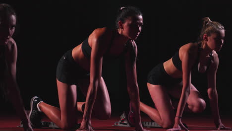 tres chicas deportivas con ropa negra del atleta por la noche en la cinta de correr comenzarán la carrera a la distancia de sprint desde la posición sentada.