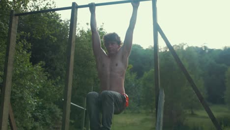 young fit topless man doing knee raise exercise to strengthen core outdoor gym slow motion