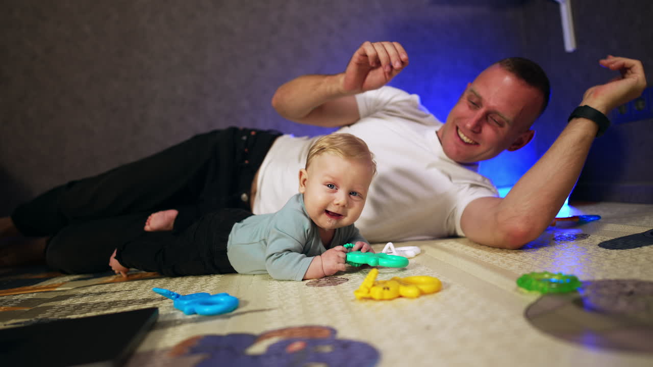 Father and infant child lying on the carpet. Smiling dad stroking his son on the head and leans to him.