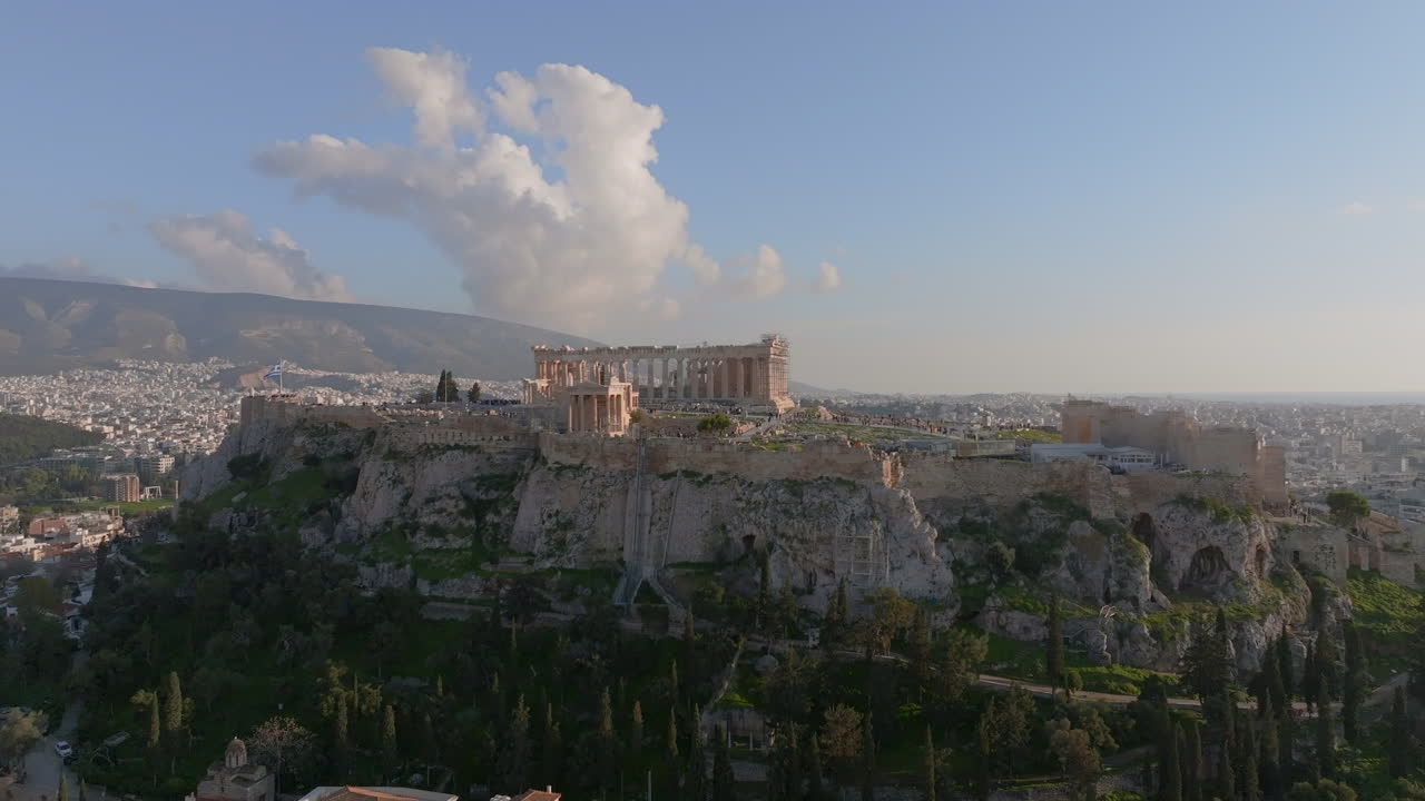Ripresa cinematografica con drone in movimento in avanti e verso l'alto che si avvicina all'Acropoli di Atene, in Grecia. Antiche rovine si ergono sopra la città in una luce calda, creando un'epica scena storica ideale per i viaggi, ecc.