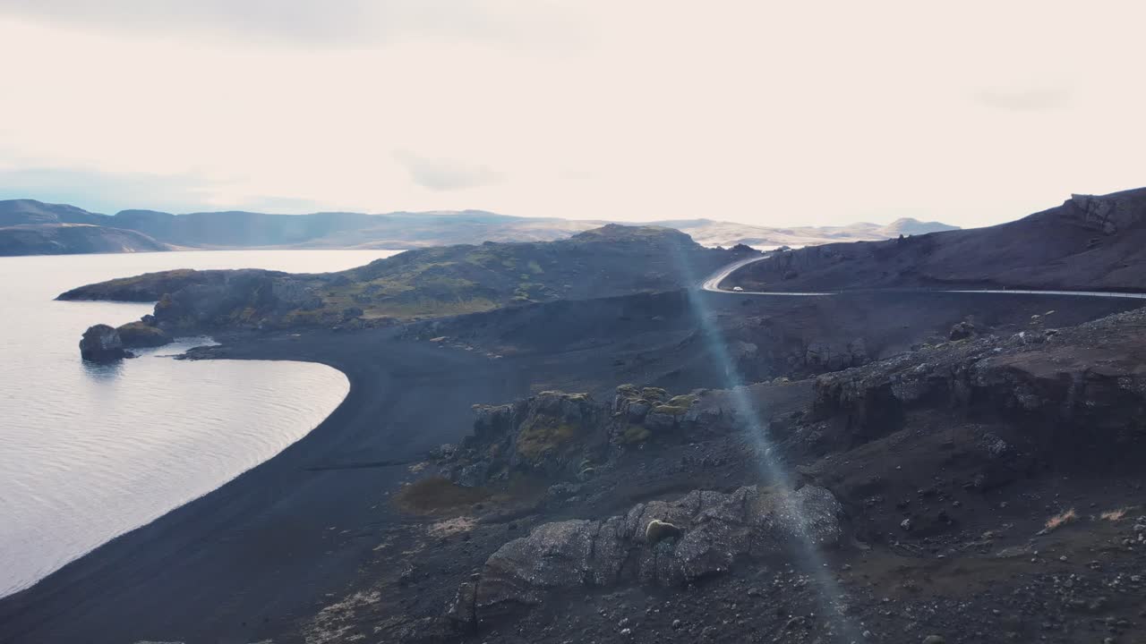 Car driving above rocky black sand beach of Kleifarvatn lake, Iceland.