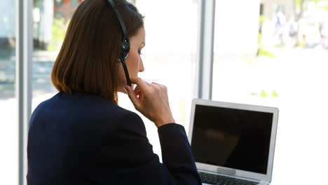 mujer de negocios hablando a través de auriculares mientras usa una computadora portátil en el escritorio 4k