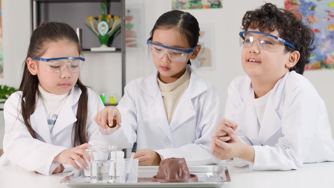 屋内で、白衣と安全ゴーグルを着用したアジア人の子供たちが、化学反応の科学実験を行っています。