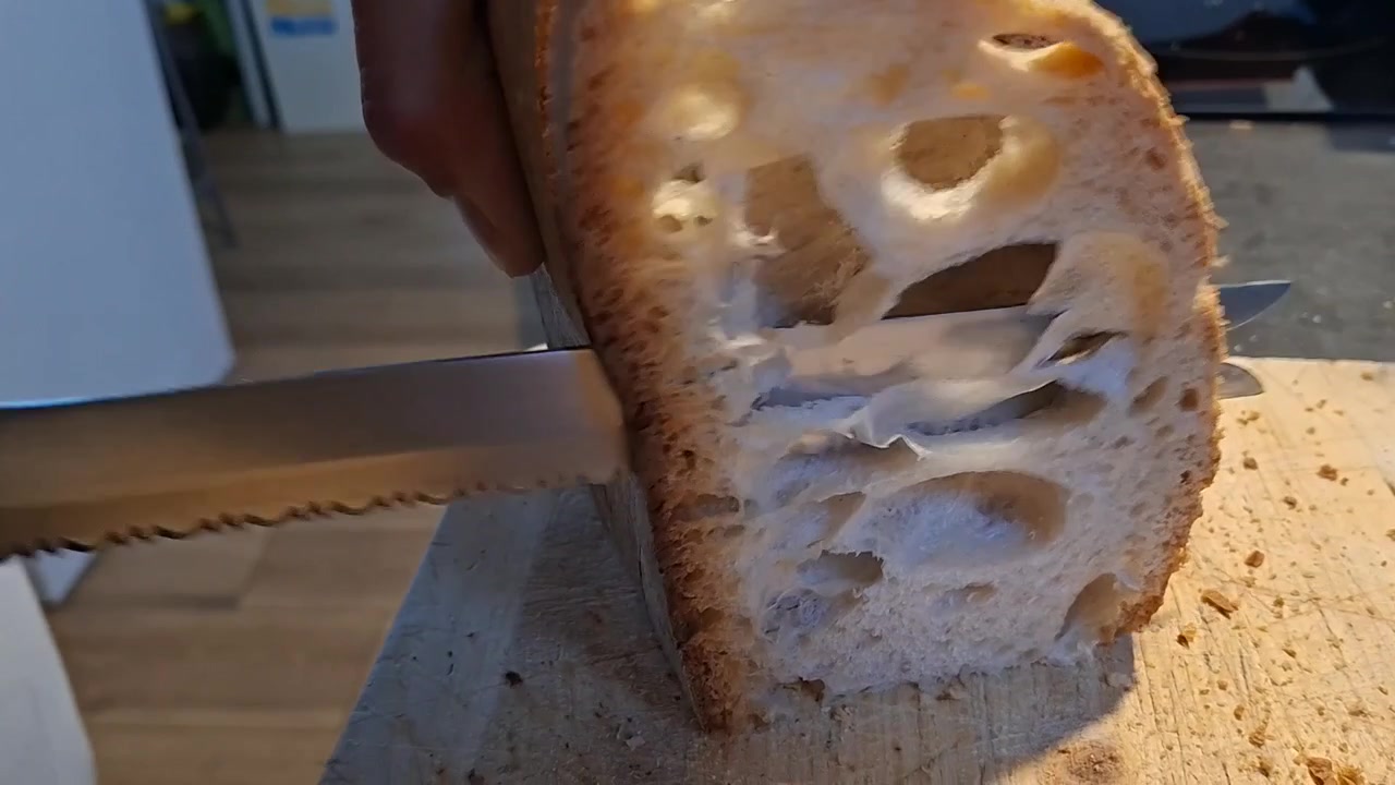 Primo piano di un uomo che affetta pane rustico italiano croccante con grandi alveoli.