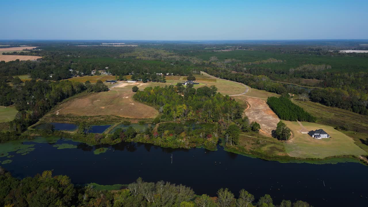 Drone pushes forward over a calm river, revealing a vineyard wedding venue surrounded by countryside and vineyard rows, creating a serene and cinematic aerial view