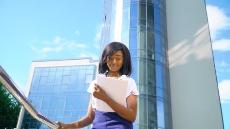 adulta afroamericana joven mujer de negocios trabaja con documentos cerca de un edificio de oficinas moderno