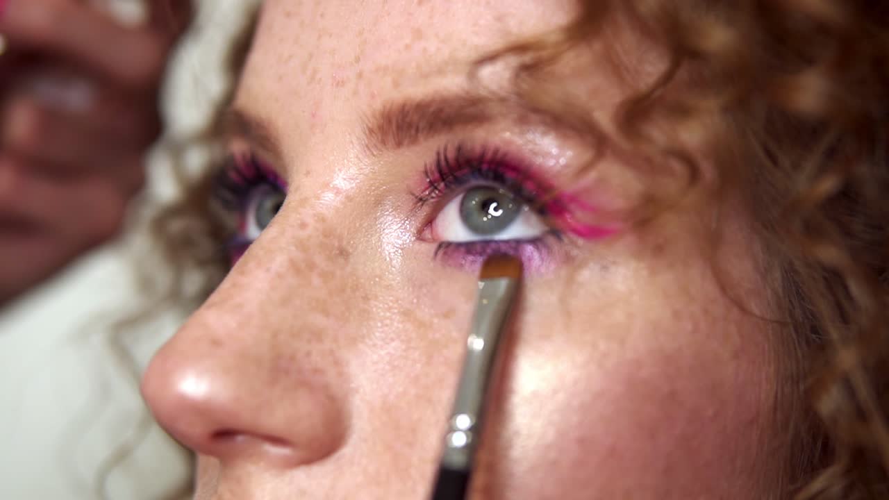 retrato de una mujer joven durante el maquillaje profesional. el maquillador aplica sombras rosas en el ojo inferior de la chica con un pincel. moda y belleza. cámara lenta
