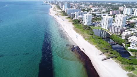 Hermosas-Vistas-Panorámicas-De-La-Playa-De-Pompano-En-Florida-Con-Edificios-De-La-Ciudad-Desde-Una-Perspectiva-Aérea-Volando-Sobre-El-Paseo-Marítimo-Con-Una-Vista-Larga-De-La-Playa-Por-Delante