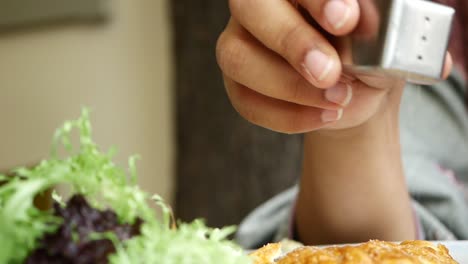 a woman sprinkles salt on a plate of food.