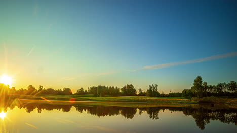 Cinematic-timelapse-of-clouds-moving-fast-over-the-sky-before-the-sun-rises-on-a-bright-day-over-a-lake-with-trees-and-grass-reflecting-in-the-calm-waters,-Time-Lapse