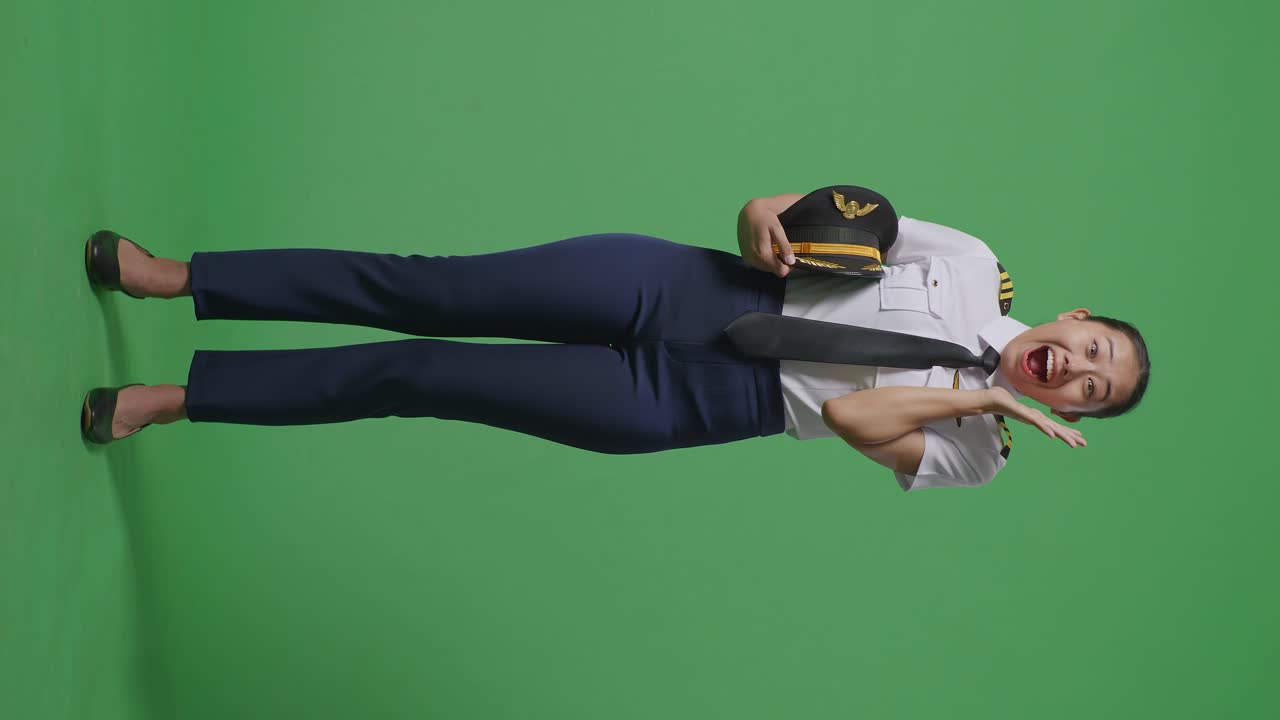녹색 스크린 배경 스튜디오에 서 있는 동안 미소 짓고 와우라고 말하는 아시아 여성 조종사의 몸이 가득 차 있습니다.
