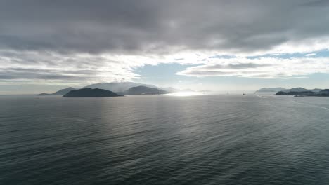 Drone video capturing Halong Bay's serene waters and lush islands under dramatic skies. Sunlight pierces through clouds, creating a mystical, tranquil early morning atmosphere.