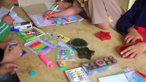 A-group-of-children-at-the-table-playing-and-drawing-colors-in-their-papers-with-pens-and-candles,-helping-them-to-be-creative-and-discover-their-talent