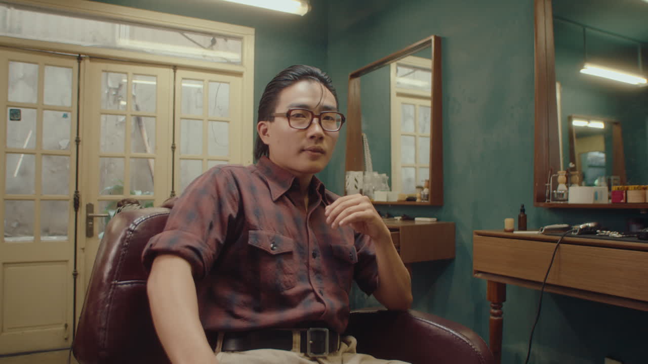 Good-Looking Asian Man Posing on Camera in Barbershop Chair