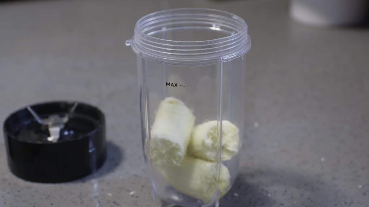 Preparazione di un frullato proteico. Mano che mette una banana nel bicchiere del frullatore.