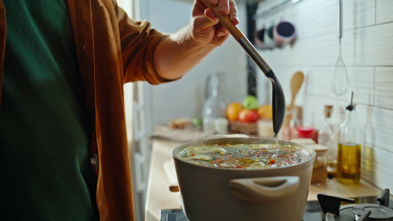 Porträt eines Mannes, der beim Suppekochen am Küchenherd telefoniert.