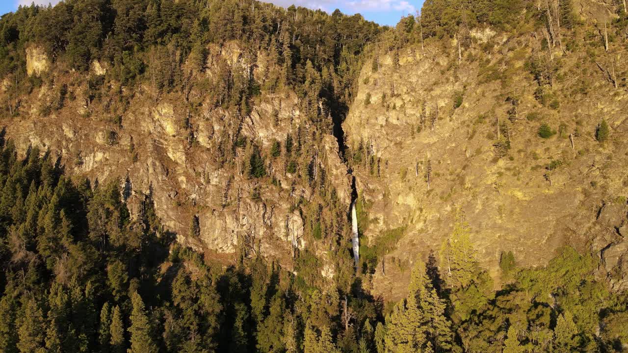 아르헨티나 파타고니아 황금시간대에 소나무 숲 산 사이에 있는 코르바타 블랑카 얇은 폭포 위로 공중 비행