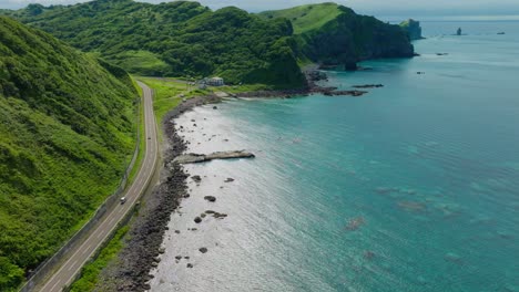 Aerial establishing drone fly above car ride in Japanese coastline road at Shakotan beach, Hokkaido, sea cliff landscape