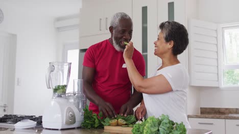 senior african american man and woman preparing fruit and vegetable health drinks at home