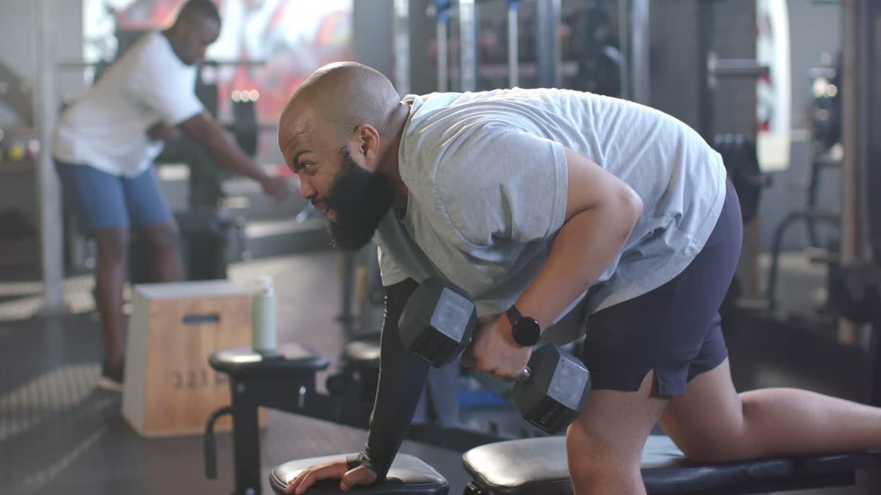 African American men, foreground man positioning on bench, pulling dumbbell, building back strength
