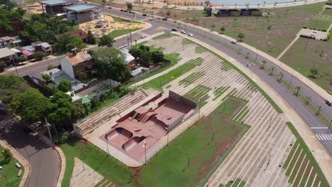 drone wide flyover of skatepark and surrounding buildings and road with passing traffic - midday