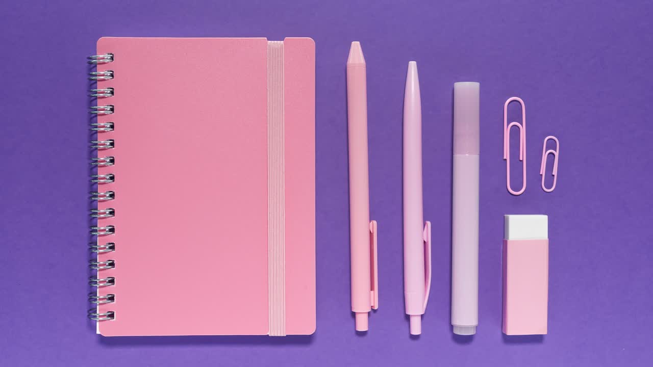 Stop motion animation shows pastel pink notebook, pens, marker, clips and eraser popping on and off a purple background for a fun back-to-school vibe