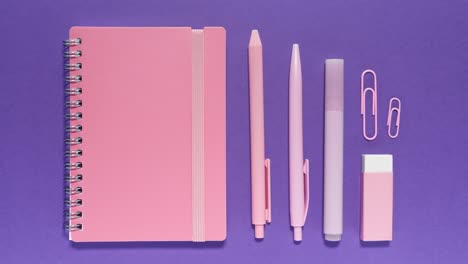 stop motion animation shows pastel pink notebook, pens, marker, clips and eraser popping on and off a purple background for a fun back-to-school vibe