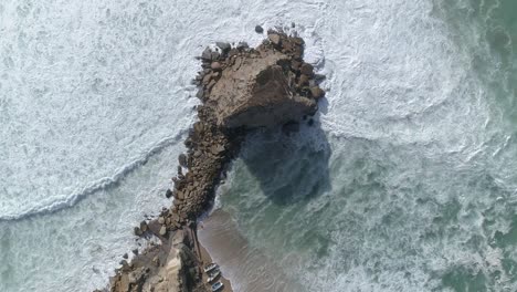 Top-aerial-drone-view-of-waves-crashing-on-rocky-coastline